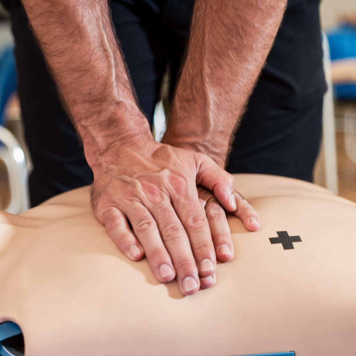 Hænder udfører hjertemassage på øvelsesdukke